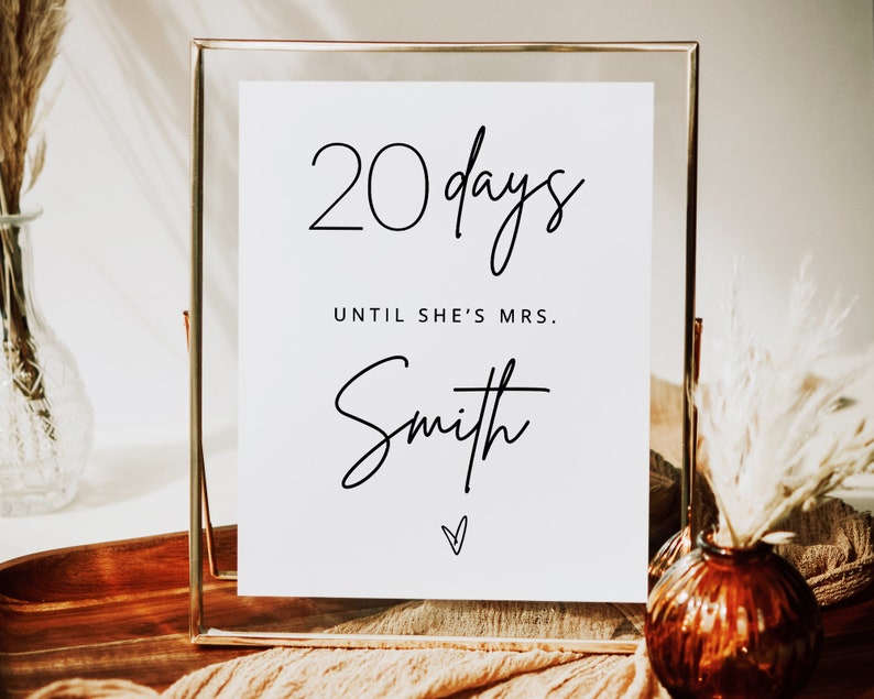May include: A white sign in a gold frame with the text "20 days until she's Mrs. Smith" in black script.