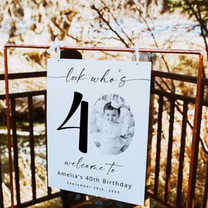 K&ouml;nnte beinhalten: Ein wei&szlig;es Schild mit schwarzem Text, der "look who's 40" lautet, mit einem Foto eines Kindes, das eine Krone und ein schwarz-wei&szlig;es Kleid tr&auml;gt. Der Text unter der Zahl lautet "welcome to Amelia's 40th Birthday September 28th, 20XX".