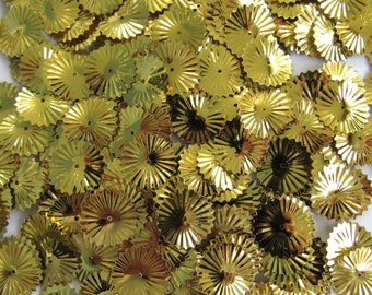 May include: A collection of small, shiny, gold-colored paper fan embellishments. Each fan has a circular center with radiating, pleated edges. The fans are scattered, creating a textured, decorative effect, suitable for crafts and scrapbooking.