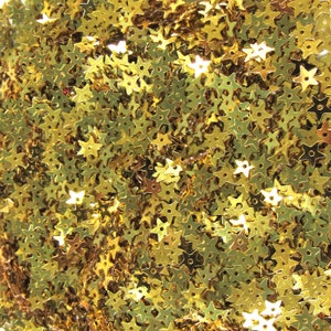 May include: A close-up shot of a collection of small, gold star-shaped confetti. The confetti is scattered, creating a dense, textured surface. The stars have a metallic sheen, reflecting light. Suitable for crafts, scrapbooking, or party decorations.