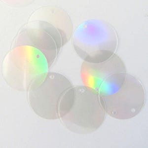May include: A collection of clear, iridescent, round sequins with small holes for stringing. The sequins have a subtle rainbow sheen, reflecting colors like green, purple, and yellow. Ideal for crafting, these sequins add a touch of sparkle.