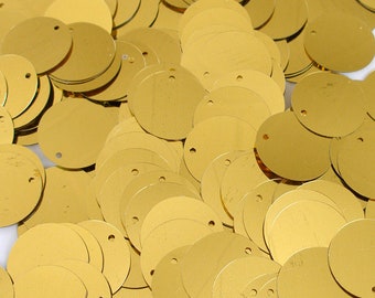 Könnte beinhalten: Nahaufnahme von zahlreichen goldfarbenen Pailletten, jede kreisförmig mit einem kleinen Loch zum Einfädeln. Die Pailletten sind verstreut und bilden eine strukturierte Oberfläche. Die goldene Farbe reflektiert das Licht und erzeugt einen hellen, schimmernden Effekt.