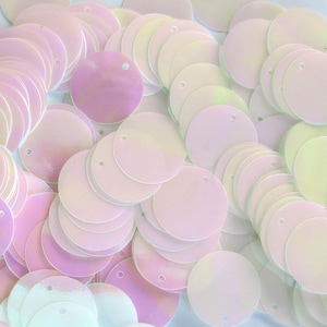 May include: A pile of iridescent, round sequins in shades of pink, lavender, and pale yellow. Each sequin has a small hole near the edge. The sequins are scattered, creating a textured, shimmering effect. Ideal for crafts and embellishments.