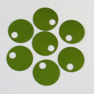 Puede incluir: Siete recortes circulares de color verde oliva dispuestos en forma de flor. Cada círculo tiene un pequeño agujero blanco cerca del borde. Los recortes están sobre un fondo blanco.