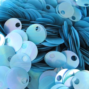 Puede incluir: Imagen abstracta de numerosas lentejuelas circulares de color azul claro, cada una con un pequeño agujero central. Las lentejuelas se superponen, creando un efecto texturizado e iridiscente. La composición destaca los detalles y las variaciones de color.