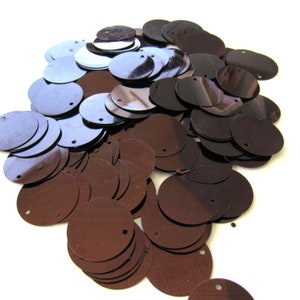 May include: A pile of brown, circular sequins with a small hole at the top. The sequins have a metallic sheen and vary slightly in color, with some appearing lighter and more reflective. These craft supplies are ideal for embellishing clothing and accessories.