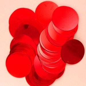 May include: A collection of circular, bright red sequins with a smooth, reflective finish. Each individual sequin is flat and round, featuring a small, centred hole for attachment. The sequins are layered and overlapping in a dense cluster.