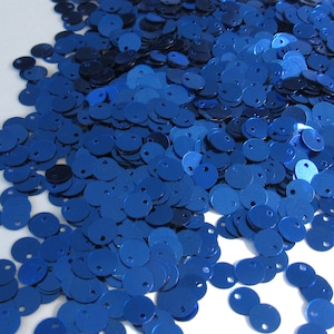 May include: A pile of shiny, round, royal blue sequins with a small hole at the top of each. The sequins are scattered across a white surface, creating a textured, reflective effect. Ideal for crafts and embellishments.