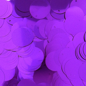 May include: A close-up shot of a pile of shiny, round, purple sequins. Each sequin has a small hole near the edge. The sequins are scattered, creating a textured, reflective surface. The color is a vibrant, saturated purple.
