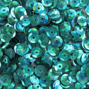 May include: A pile of iridescent teal sequins. Each sequin is round with a hexagonal shape and a hole in the center. The sequins have a shiny, reflective surface, with hints of blue and green. These craft supplies are ideal for embellishing clothing and accessories.