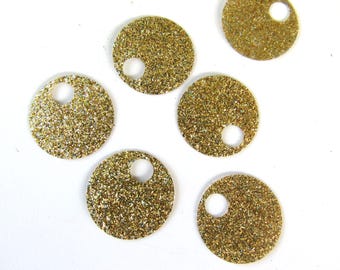 May include: Six gold glittered round charms with a small hole near the top. The charms are scattered on a white surface. These decorative charms are ideal for jewelry making or other craft projects.