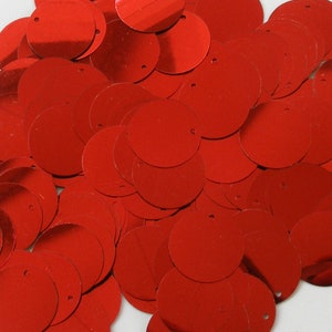 May include: A close-up of numerous red, circular sequins. Each sequin has a small hole for sewing. The sequins are scattered, overlapping, creating a textured surface. The color is a bright, solid red.