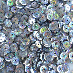 May include: A collection of iridescent silver sequins. Each sequin is circular with a central hole and a faceted, reflective surface. The sequins shimmer, displaying a spectrum of colours.