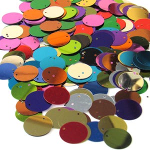 Puede incluir: Un conjunto de lentejuelas redondas multicolores, en tonos rosa, verde, naranja, azul y dorado. Cada lentejuela tiene un pequeño agujero para coser o manualidades. Las lentejuelas están dispersas, creando una apariencia vibrante y texturizada, ideal para adornos.