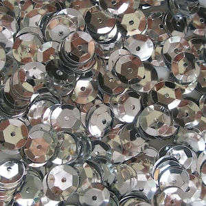 May include: A close-up of a pile of silver sequins. Each sequin is hexagonal with a small central hole. The sequins are reflective, creating a sparkling effect. They are scattered randomly, filling the frame. Ideal for craft projects.