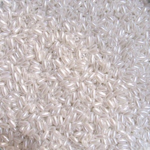 May include: A close-up shot of a pile of iridescent white oval-shaped beads. The beads have a pearlescent sheen, reflecting light and creating a shimmering effect. These beads are ideal for jewelry making and craft projects.