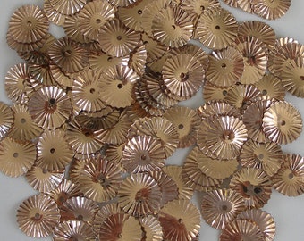 May include: A collection of small, metallic gold-colored sequins. Each sequin has a circular shape with a central hole and a ridged, sunburst-like design radiating outwards. These decorative sequins are ideal for embellishing crafts and clothing.
