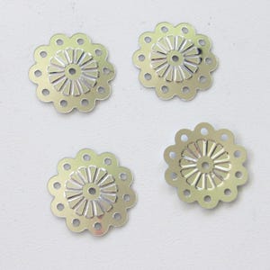 May include: Four silver-colored, flower-shaped metal embellishments. Each has a scalloped edge with small holes and a detailed center design. These decorative pieces are ideal for crafts and jewelry making.