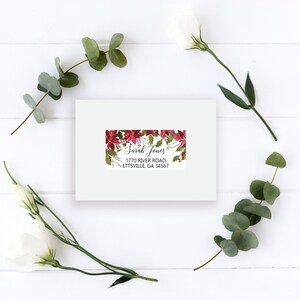 May include: A rectangular white mailing label featuring a festive red poinsettia and green holly leaf border. The label displays the printed text Sarah Jones, 1770 River Road, Ettsville, GA 34567 in a black serif and script font.