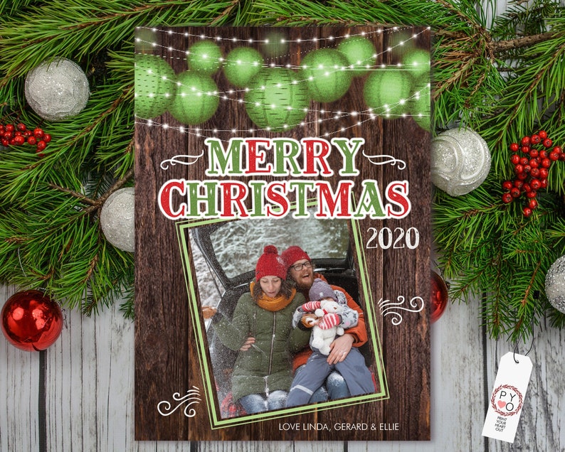 Pu&ograve; includere: Un biglietto di Natale con sfondo in legno, con la scritta "MERRY CHRISTMAS 2020". Il biglietto include una foto di famiglia all'interno di una cornice bordata di verde. Ornamenti verdi e luci di stringa in alto. In basso c'&egrave; scritto "Love Linda, Gerard & Ellie".