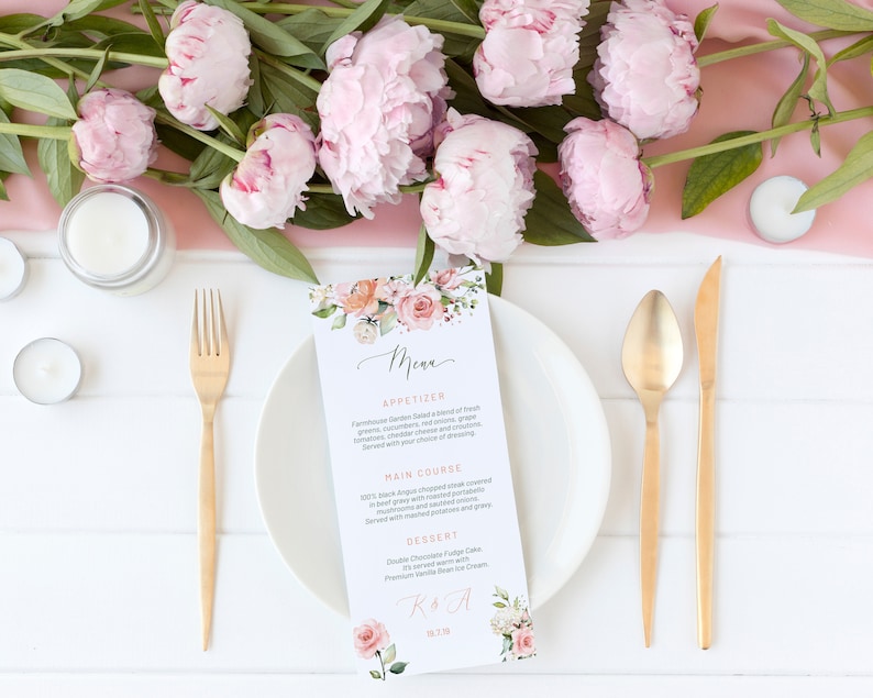 May include: A wedding menu with a floral design and gold calligraphy. The menu lists appetizers, main course, dessert, and the couple's names. The menu is placed on a white table with a pink tablecloth and gold silverware.