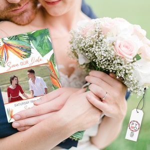 May include: A tropical-themed save the date card with a photo of a couple in the background. The card features a colorful bird of paradise flower and green leaves. The text "Save Our Date" is written in orange script. The date "Saturday 18th" is written below the photo.
