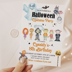 Op de afbeelding: Halloween-verkleedfeestuitnodiging met aquarel illustraties van geesten, vleermuizen en andere spookachtige personages. De uitnodiging is voor Cassidy's 8e verjaardag, met datum, tijd en locatie. De uitnodiging wordt in een hand gehouden.