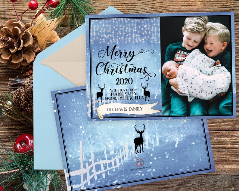 May include: Christmas card with a blue and white winter scene, featuring the text "Merry Christmas 2020" and a family photo. The card includes a light blue envelope and decorative elements like pinecones and berries.