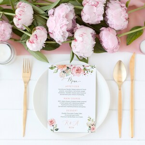 May include: A wedding menu card with a floral design featuring pink and peach flowers. The menu includes appetizers, main course, and dessert. The card also includes the couple's initials and wedding date.