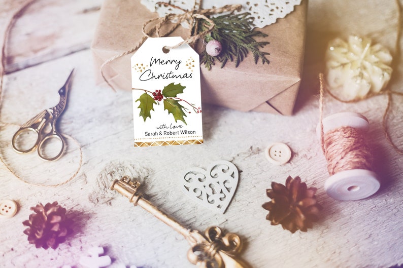 Może przedstawiać: Zapkowany prezent z etykietą z napisem &bdquo;Merry Christmas&rdquo; z ostrokrzewem i jagodami. Scena obejmuje nożyczki, klucz, serce, guziki i szpulkę sznurka, wszystko na rustykalnej drewnianej powierzchni.