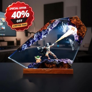 Peut inclure: Un objet décoratif en résine et bois représentant une figurine de personnage en armure tirant un rayon d'énergie jaune, avec une petite créature verte à côté. La scène est encastrée dans un cadre en résine translucide bleue et violette.