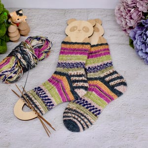 Könnte beinhalten: Ein Paar bunte gestreifte Socken auf hölzernen Panda-Sockenspannern. Die Socken sind mit verschiedenen Farben gestrickt, darunter Rosa, Grün, Orange und Blau.