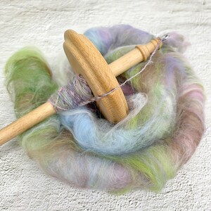 May include: A wooden spinning wheel with a spindle and a skein of colorful yarn. The yarn is a mix of pink, blue, green, and brown.