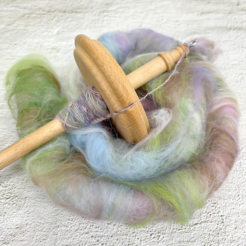 May include: A wooden spinning wheel with a spindle and a skein of colorful yarn. The yarn is a mix of pink, blue, green, and brown.