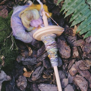 May include: A wooden spinning wheel with a colorful yarn ball and a skein of yarn. The yarn is a mix of purple, blue, yellow, and pink.