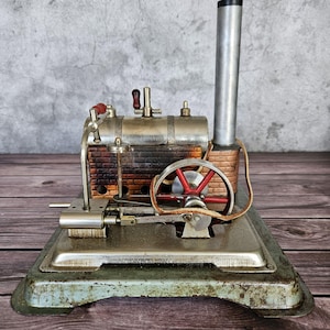 May include: A vintage steam engine model with a silver boiler, red and brown accents, and a red flywheel. The model sits on a rectangular base with a distressed, aged appearance. The chimney is tall and silver.