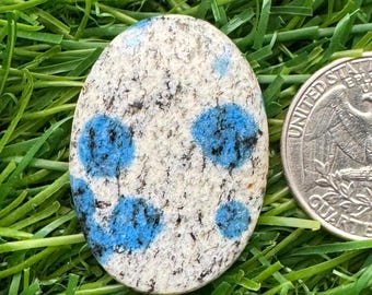 May include: A white and blue oval-shaped stone with a speckled pattern. The stone is about the size of a US quarter.