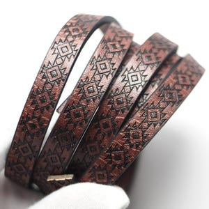 May include: A rolled-up brown leather bracelet with a geometric pattern. The bracelet is made of several thin strips of leather, each with a repeating design of diamonds and triangles. The leather has a slightly metallic sheen.