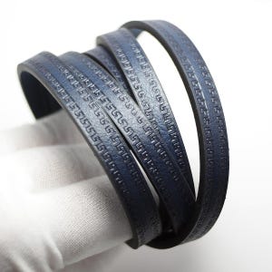 May include: A navy blue leather bracelet with a repeating geometric pattern. The bracelet is coiled, displaying the detailed design and texture. The leather has a subtle sheen, suggesting high quality. The bracelet is a stylish accessory.