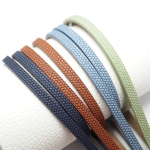 Puede incluir: Cinco cordones de cuero de diferentes colores, cada uno con una superficie texturizada. Los colores son verde salvia, azul claro, azul marino, marrón y óxido.