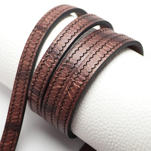 May include: Brown leather cord with a decorative stitched pattern. The cord is rolled up and has a textured surface.
