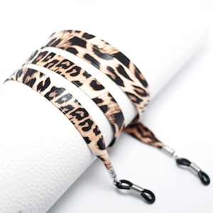 May include: A pair of leopard print glasses straps with black and silver metal clasps. The straps are made of a soft, flexible material and are designed to keep your glasses secure.