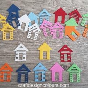 May include: A collection of small, flat, die-cut house shapes in various colours including red, blue, yellow, green, orange, pink, and white. Each house features a simple roof, a rectangular door opening, and horizontal slats. Text reads craftdesigncolours.com.
