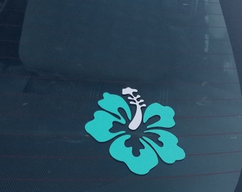 Może przedstawiać: Naklejka z turkusowym hibiskusem z białym środkiem, przyklejona do szyby samochodu.