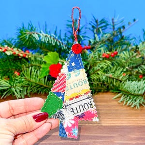 Peut inclure: Ornement de sapin de Noël fait à la main. L'arbre est composé de morceaux de tissu colorés, avec des motifs et des couleurs unies. Il y a un bouton rouge en haut et une boucle rouge pour l'accrocher. En arrière-plan, des branches de conifères et une surface en bois.