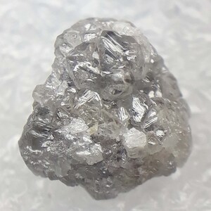 Può includere: Un cristallo di diamante naturale, grigio e grezzo, con una cima appuntita e molte sfaccettature.