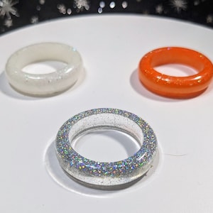 May include: Three resin rings, one white, one orange, and one clear with iridescent glitter.