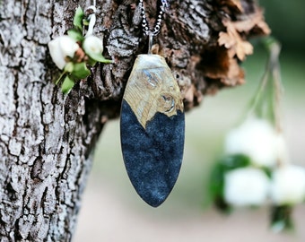 May include: A black and gold resin pendant with a wood grain pattern hangs from a silver chain. The pendant is oval shaped and has a smooth, polished finish.