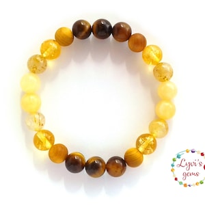 Puede incluir: Una pulsera de cuentas redondas y pulidas en tonos amarillos, ámbar y marrón. Las cuentas están ensartadas, creando un efecto degradado. La pulsera presenta una mezcla de piedras opacas y translúcidas. La banda elástica permite un ajuste flexible y cómodo.