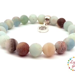 May include: A light green, brown, and white gemstone bracelet with a silver lotus charm. The bracelet is made of round beads and is approximately 7 inches in length.